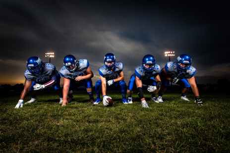football players in blue jersey lined under grey white cloudy sky during sunset